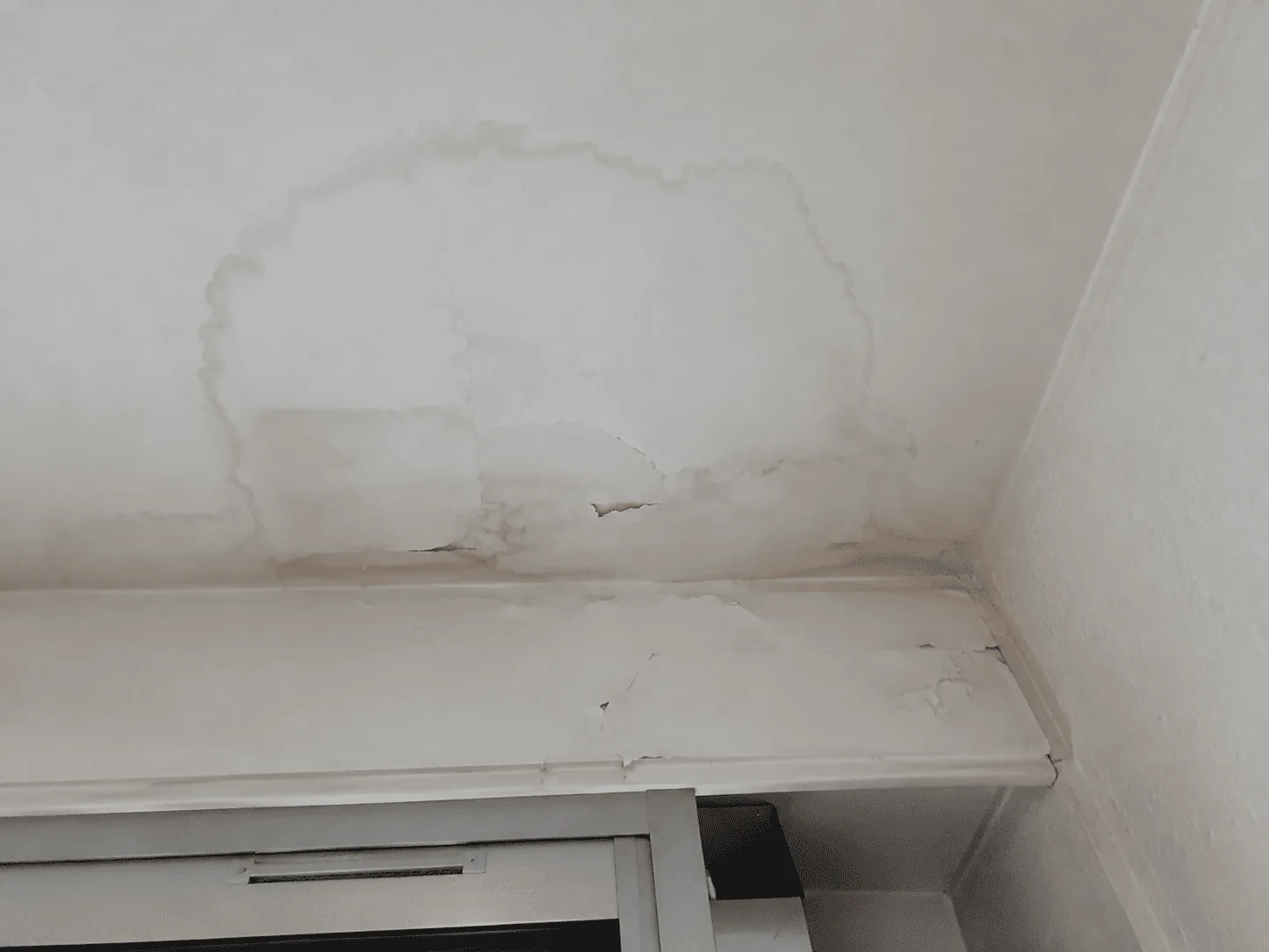 Un dégât des eaux est visible au plafond et au-dessus d’une fenêtre.