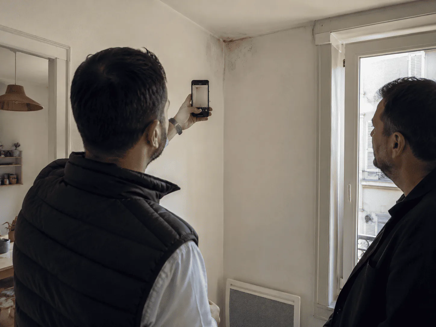 Deux personnes documentent une trace d’humidité dans un logement.